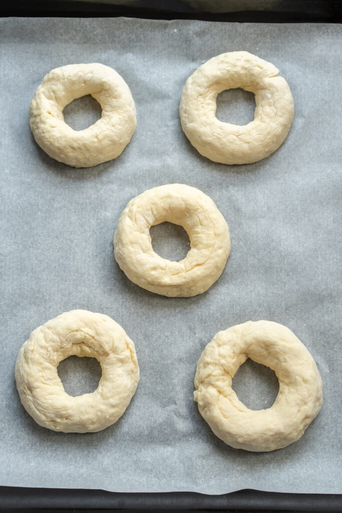 Unbaked Greek yogurt bagels arranged on a baking sheet with parchment paper