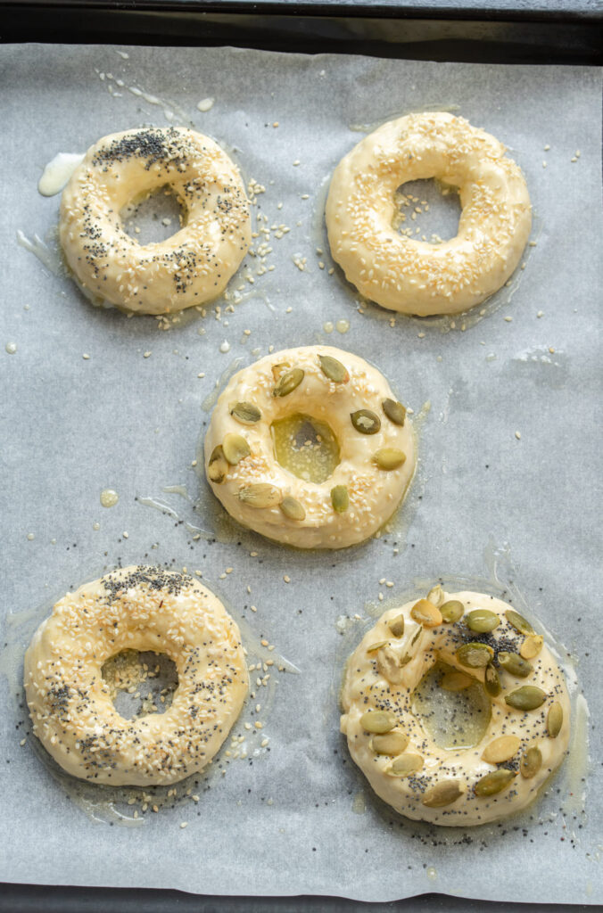 Unbaked bagels brushed with butter and sprinkled with seeds
