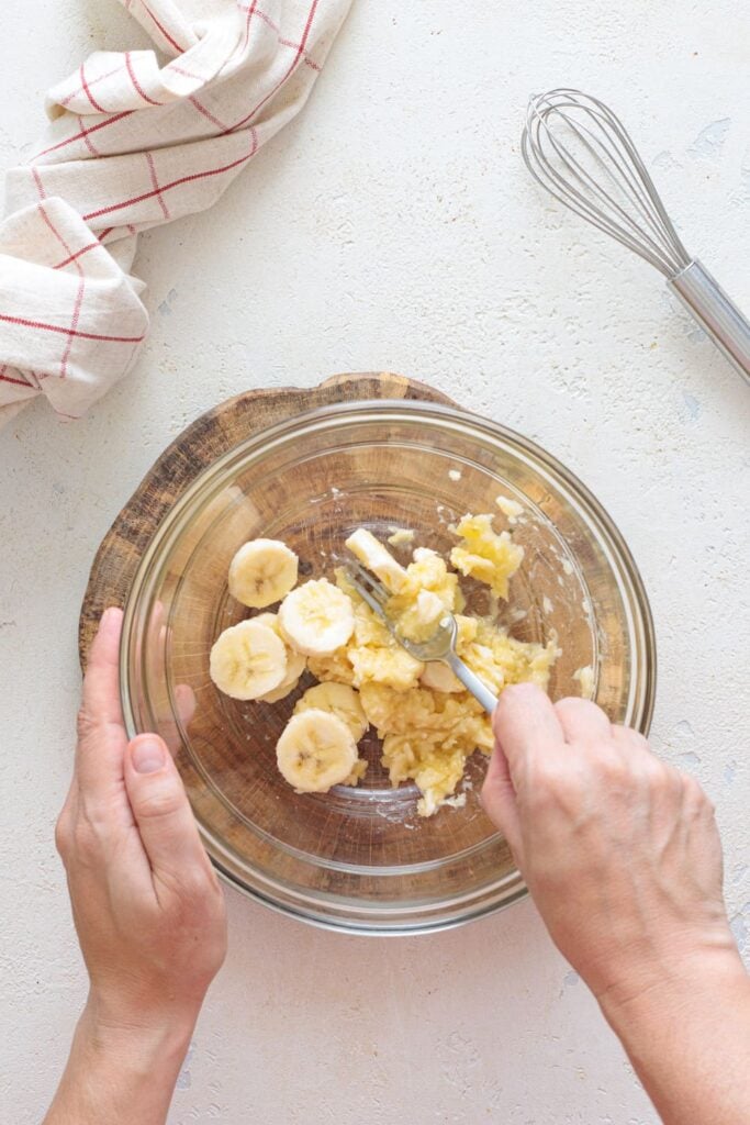 Mashing sliced bananas with a fork in a glass bowl for pancake batter