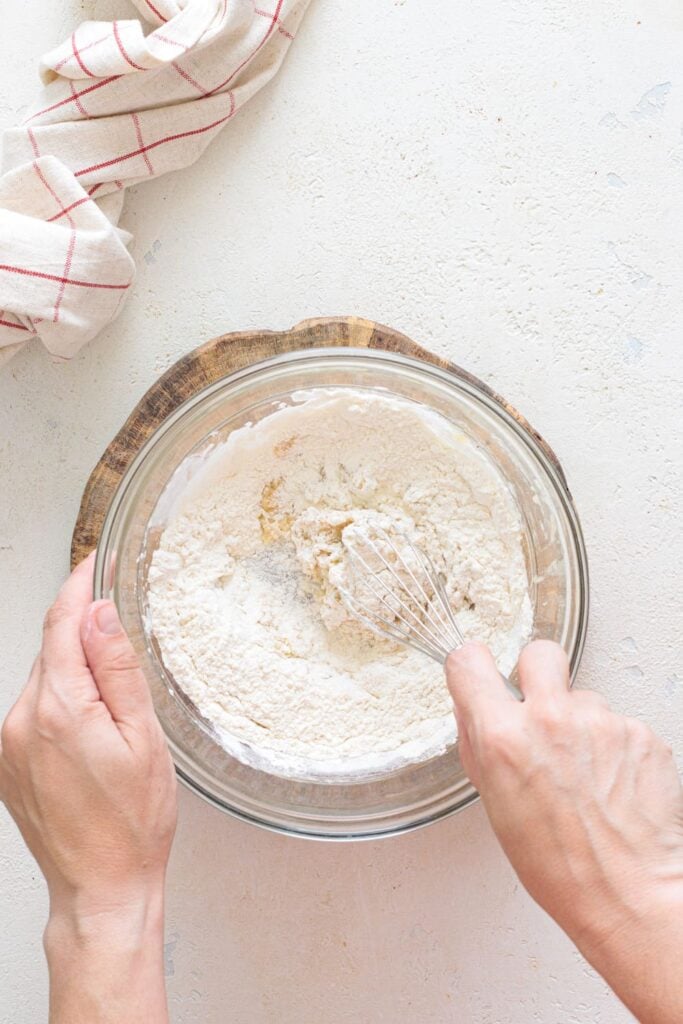 Adding flour to mashed banana mixture in a glass bowl with whisk