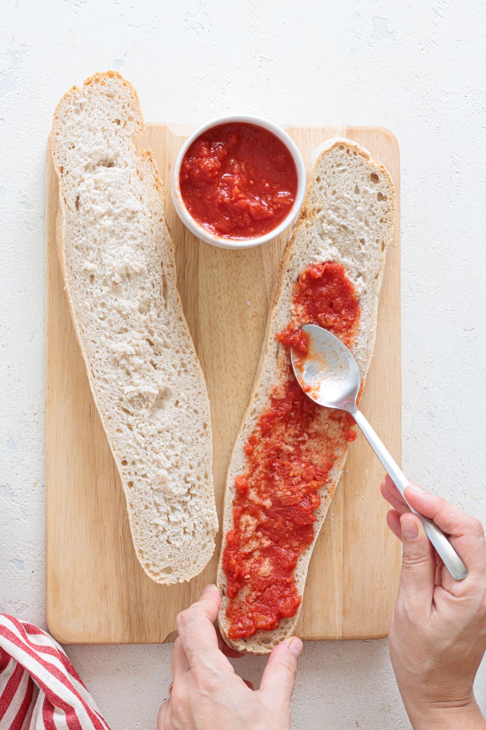 Spreading tomato sauce on sliced baguette to start the pizza base