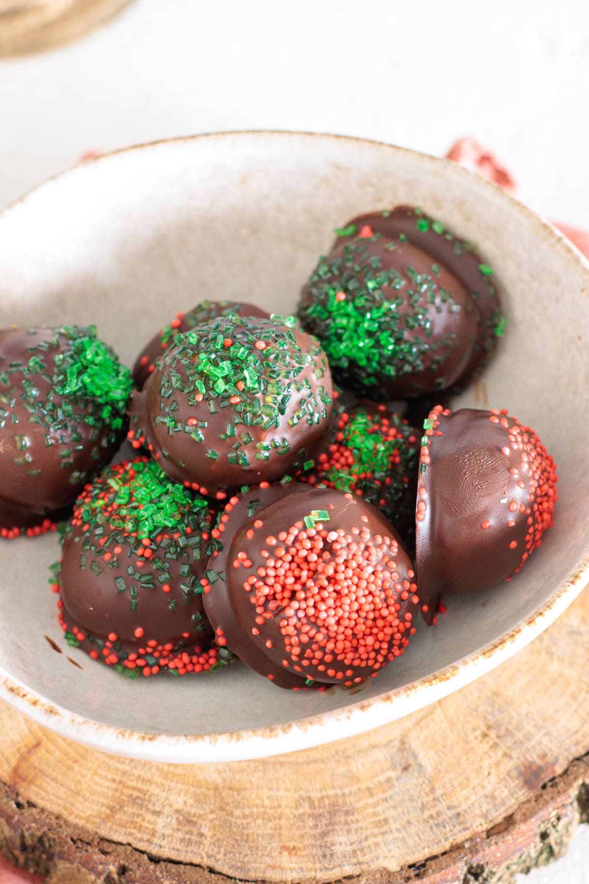 Finished peanut butter balls coated in dark chocolate and topped with red and green sprinkles for a holiday touch.