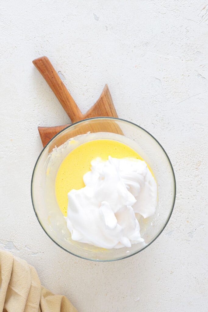 Stiff egg whites added to egg yolk mixture in a bowl for keto bread batter