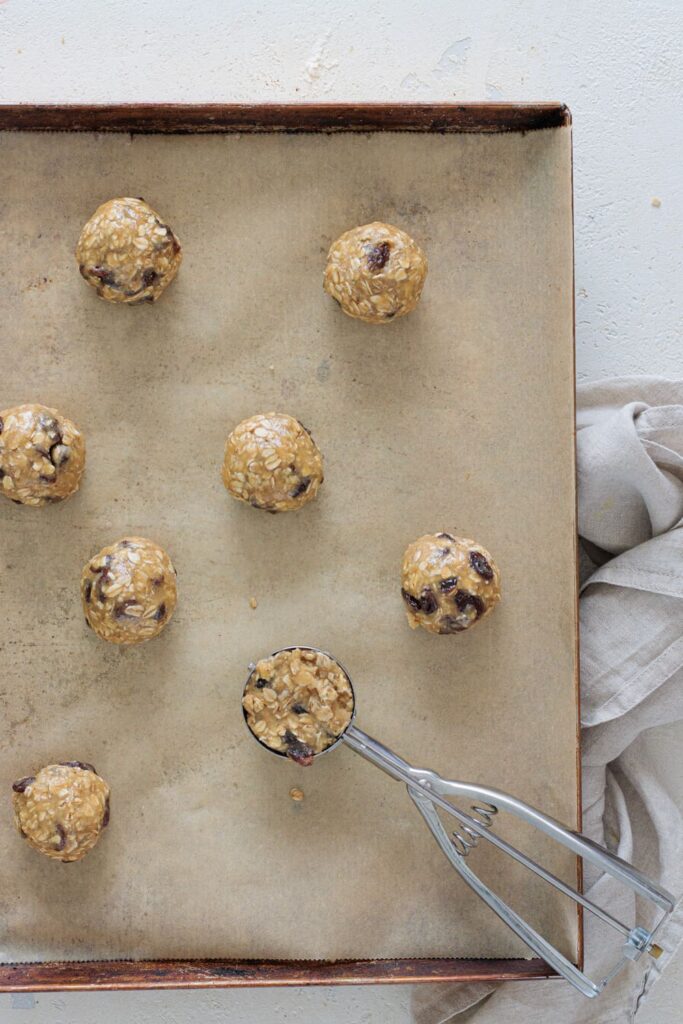 Cookie dough balls scooped onto a baking sheet with raisins and oats