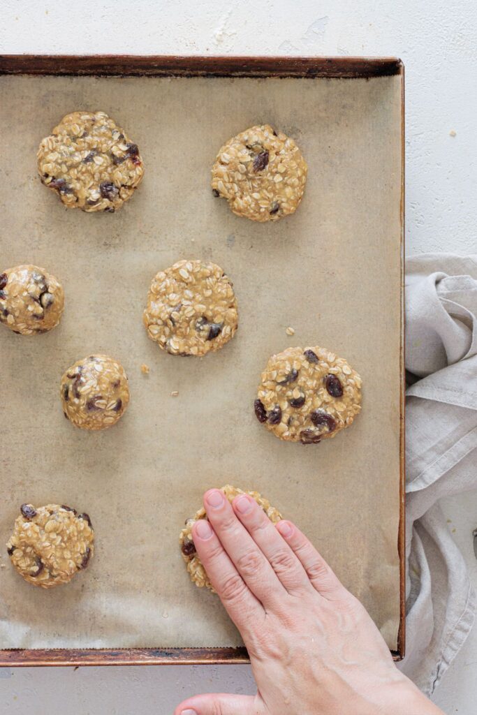 Flattening oatmeal raisin cookie dough balls by hand before baking