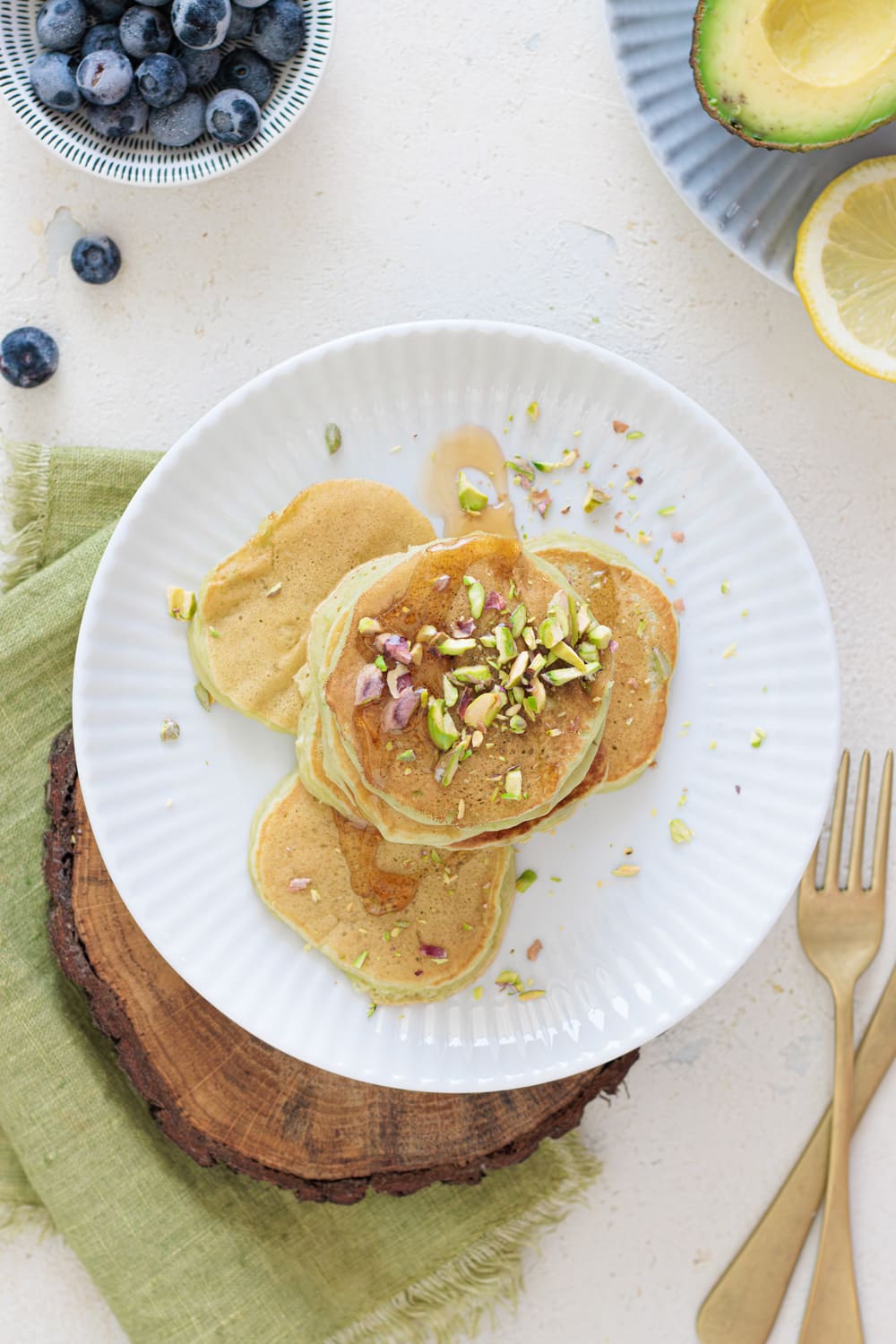 Stack of avocado banana pancakes topped with chopped pistachios and drizzled with syrup on a white plate.