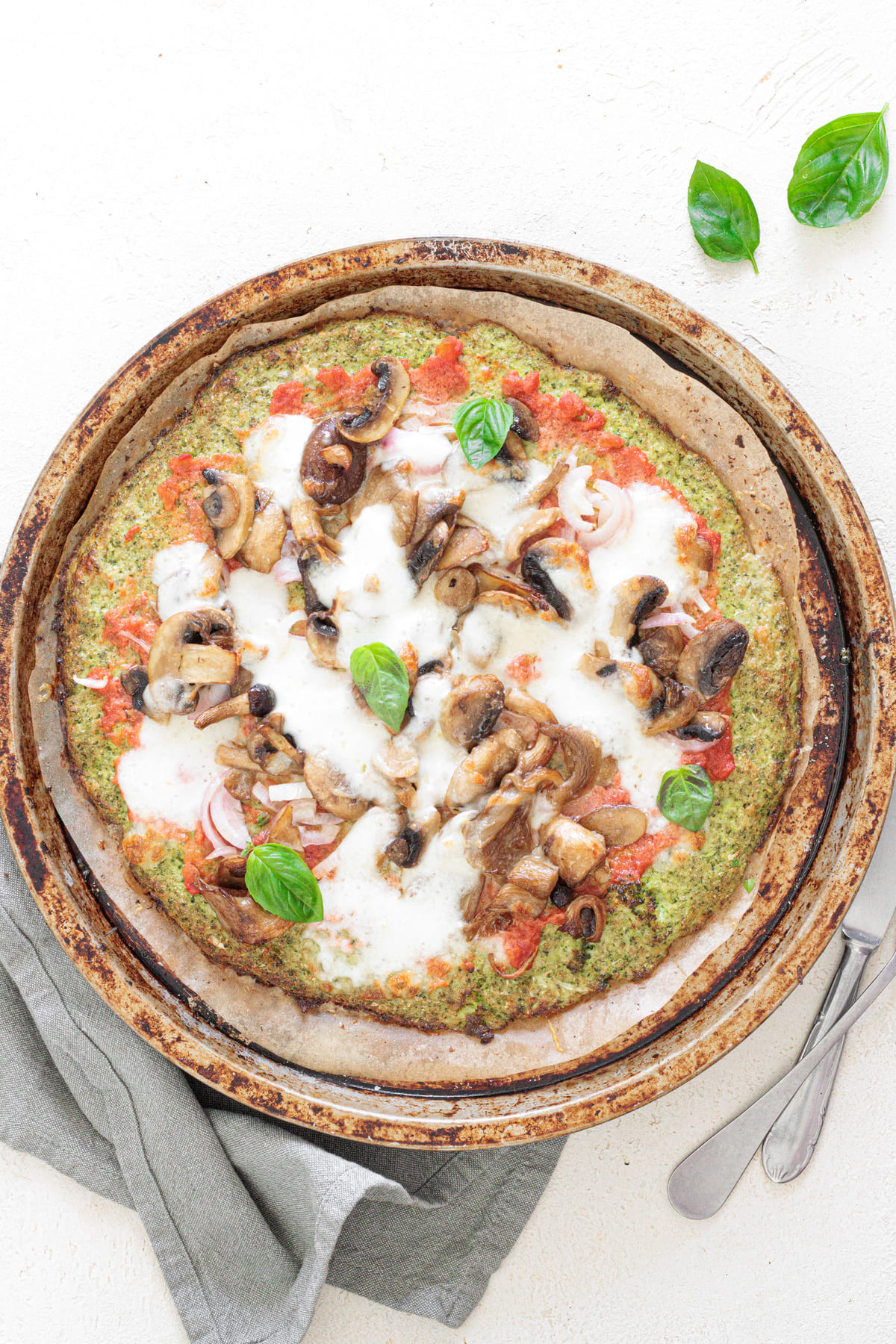 Baked broccoli crust pizza topped with mushrooms, melted mozzarella, and fresh basil leaves