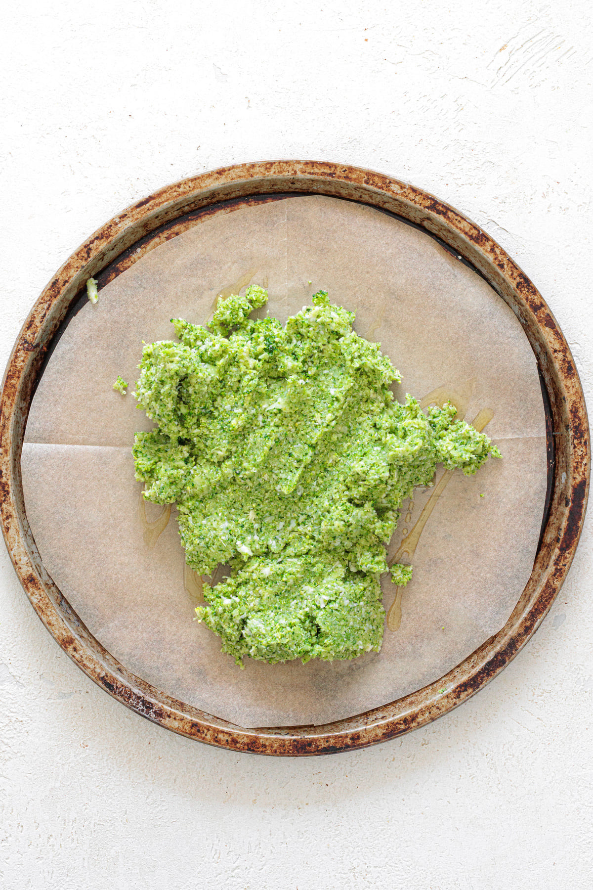 Broccoli pizza crust mixture placed on a round baking tray lined with parchment paper