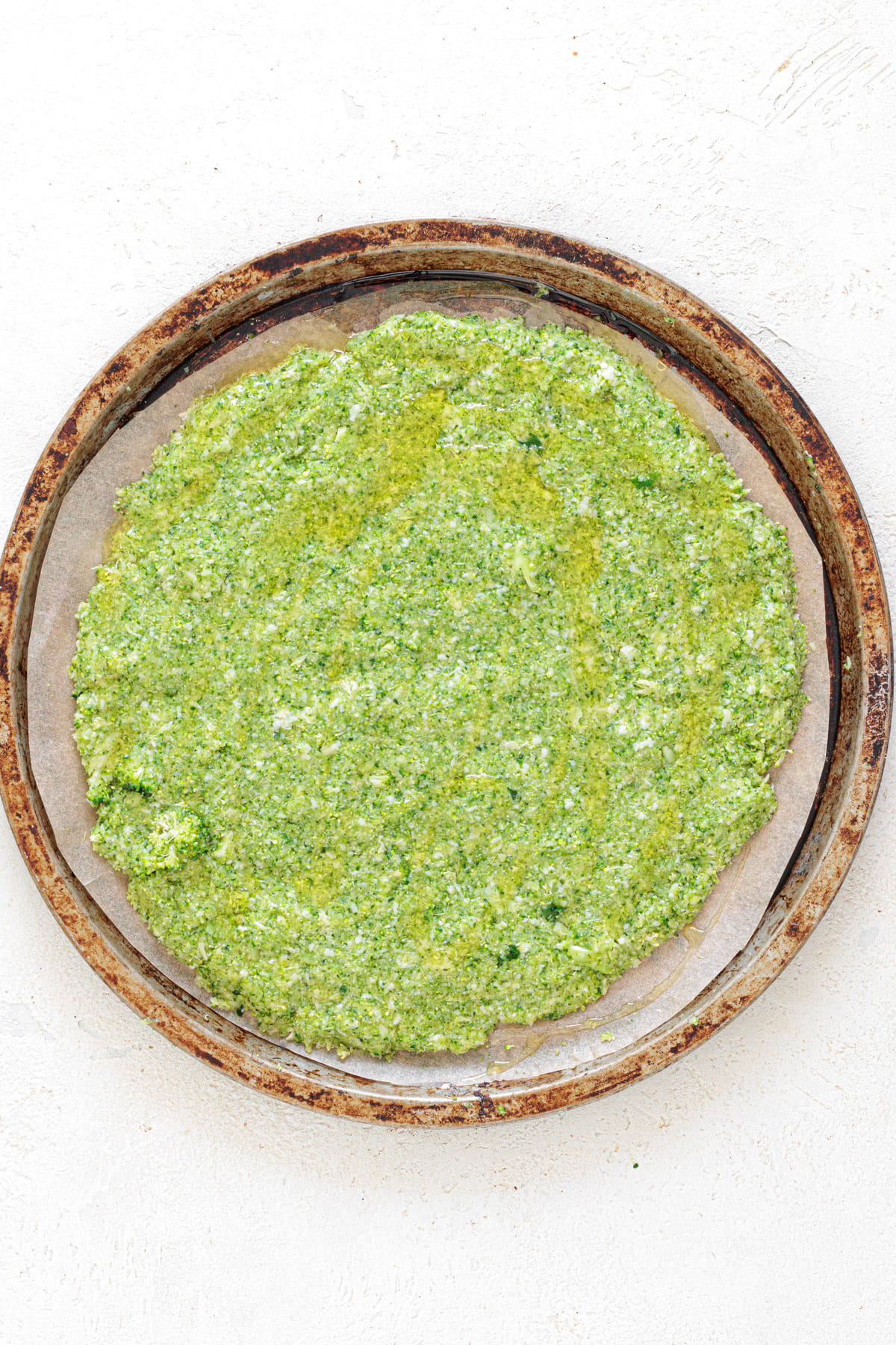 Broccoli mixture evenly spread into a round pizza crust on a baking tray, ready to bake