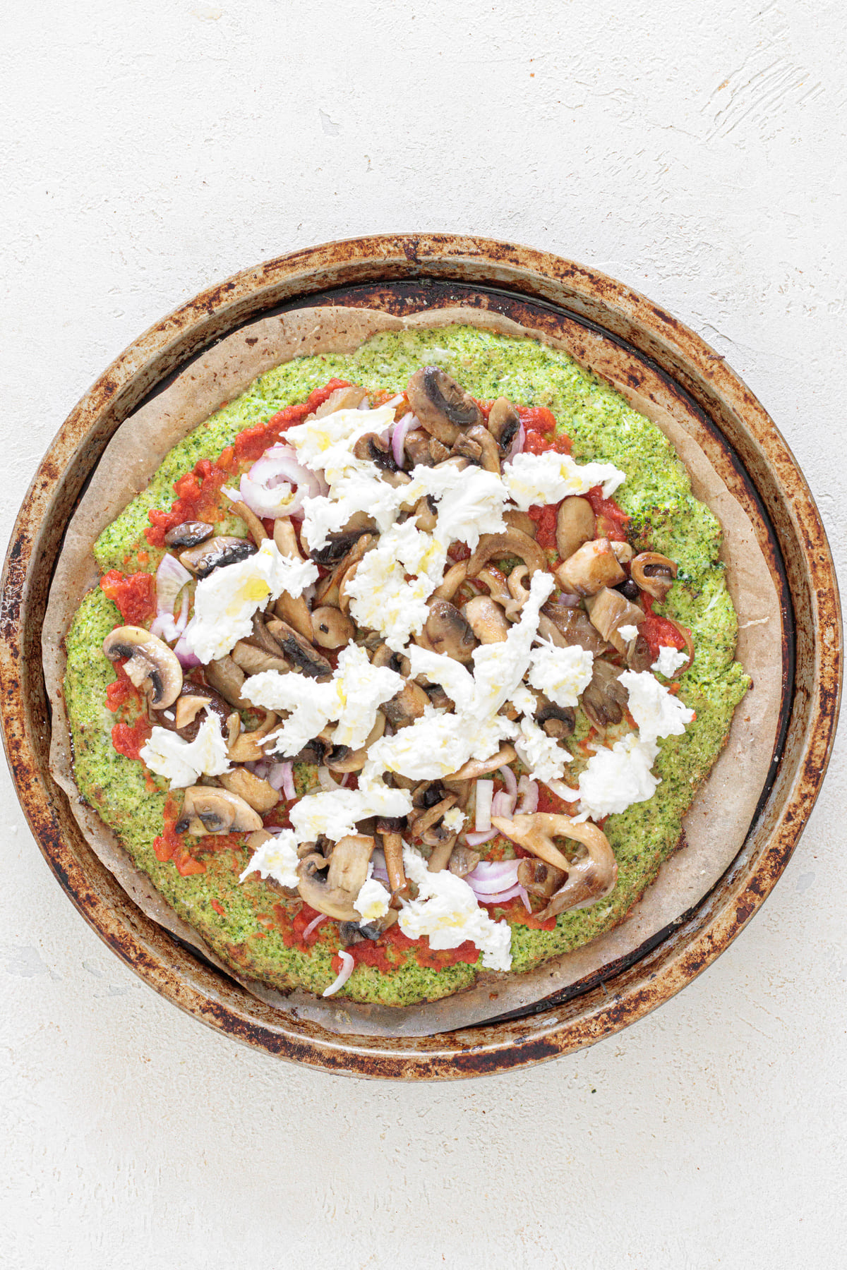 Broccoli crust pizza topped with tomato sauce, mozzarella, and sautéed mushrooms before baking