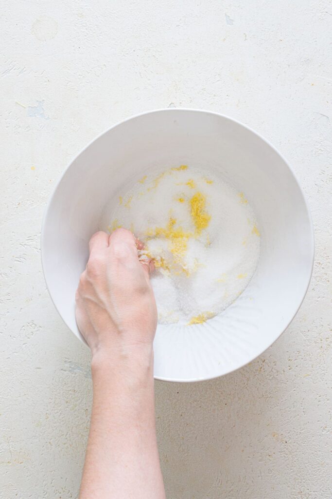 Rubbing sugar and lemon zest together in white bowl with fingers