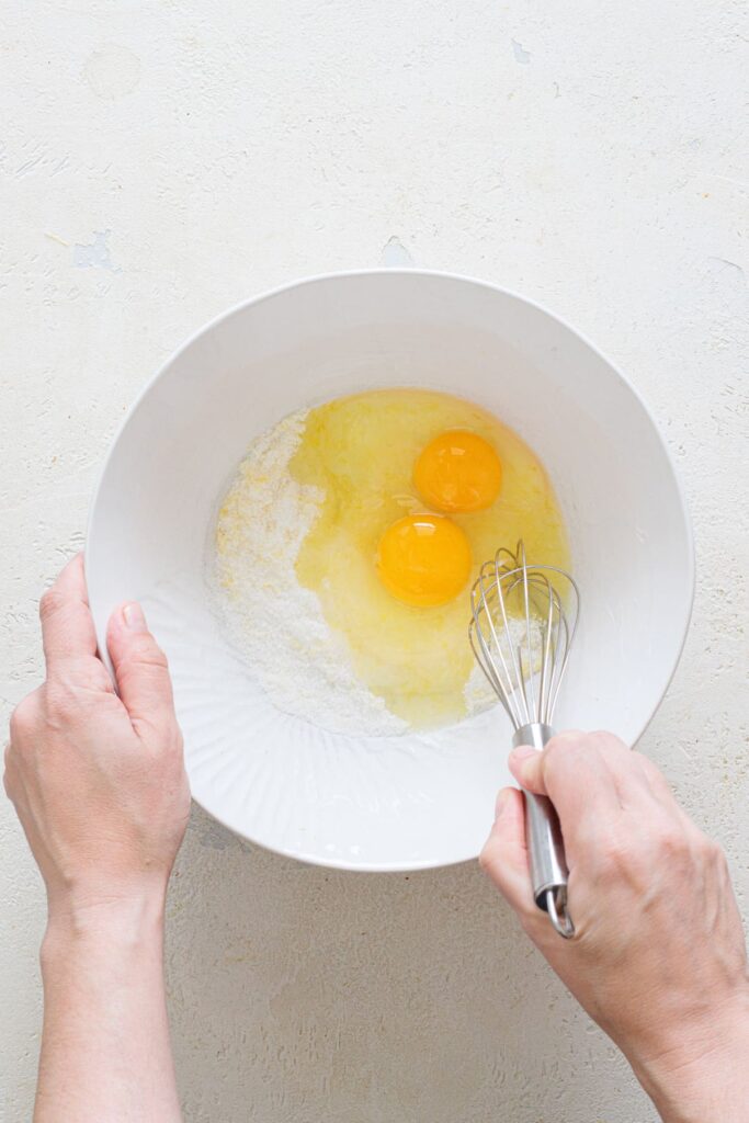 Whisking eggs into lemon sugar mixture in a bowl