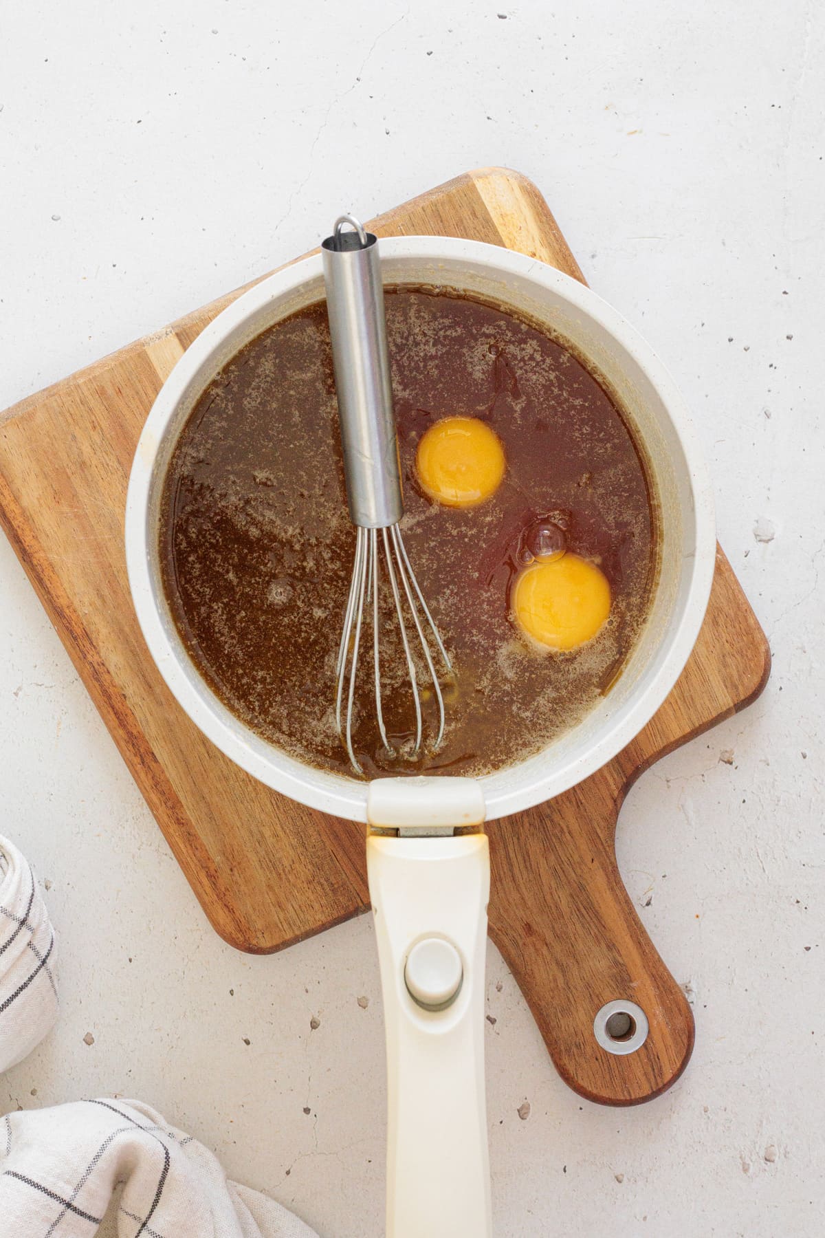 Two eggs added to the syrup mixture in a saucepan with a whisk.
