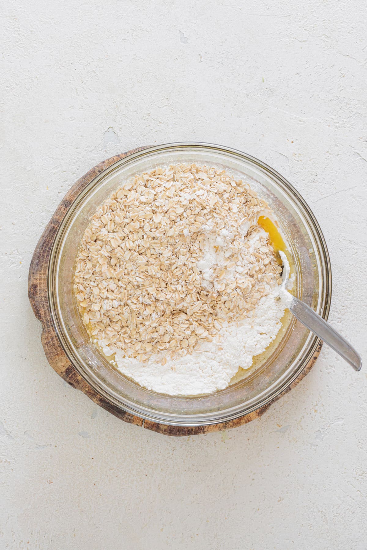 Bowl with flour, oats, and baking soda on top of the wet cookie mixture