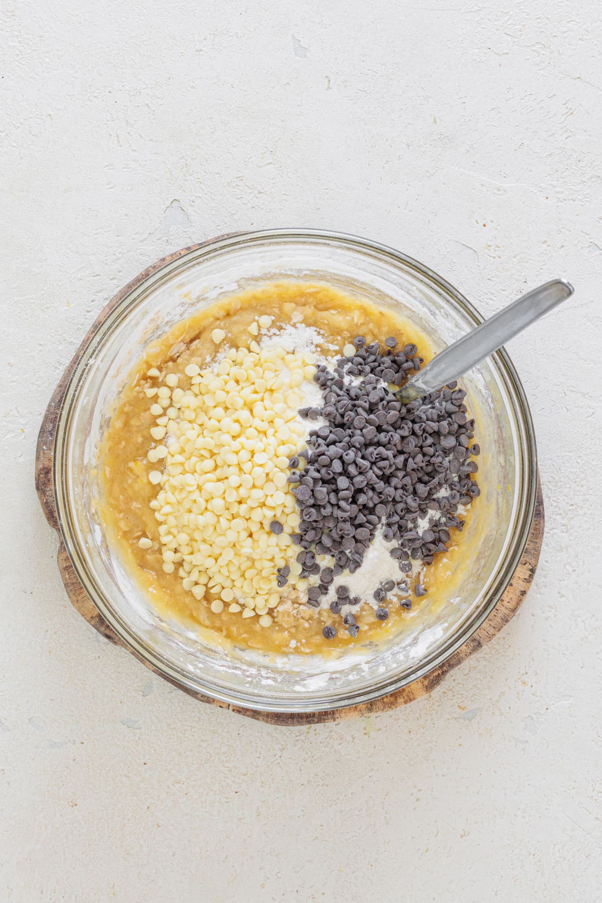 Mixing white and dark chocolate chips into cookie dough in a glass bowl