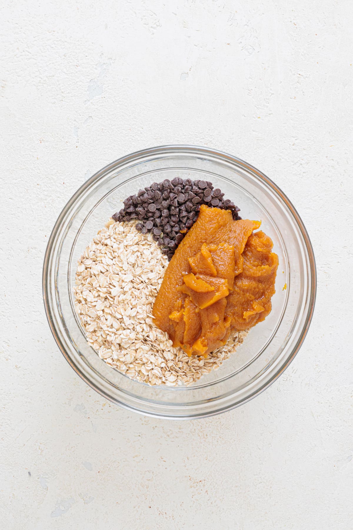 Pumpkin mixture added to a bowl of oats, chocolate chips, and pumpkin spice