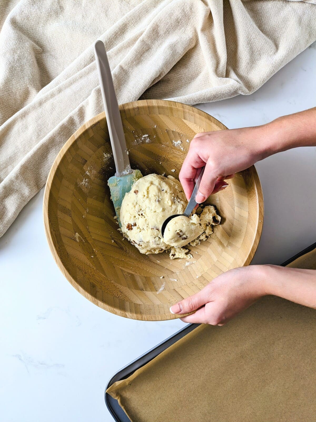 Scooping cookie dough from a wooden bowl with a small spoon