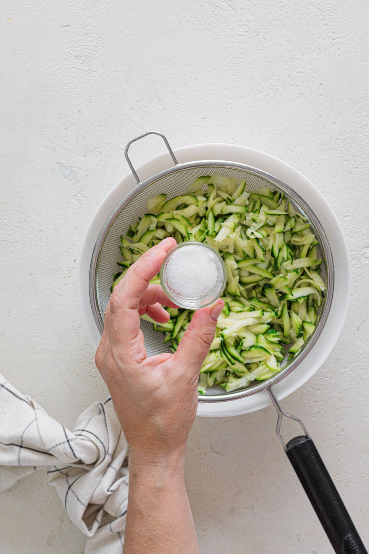 Hand sprinkling salt over grated zucchini in a strainer