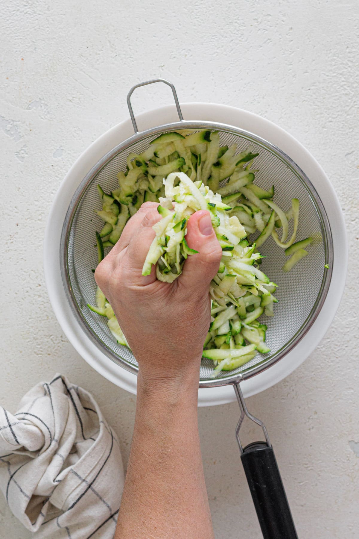 Hand squeezing grated zucchini to remove water