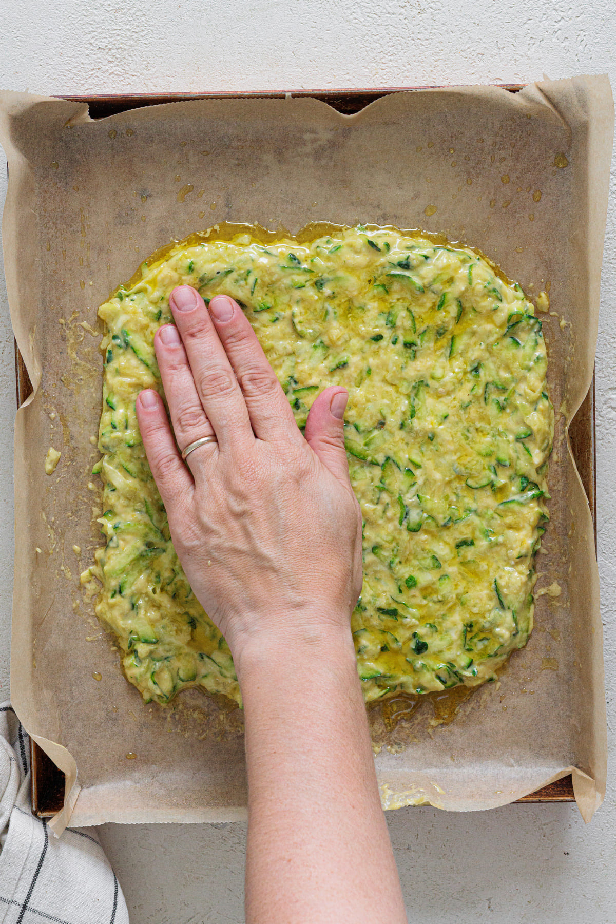Hand pressing zucchini batter onto a baking tray lined with parchment paper
