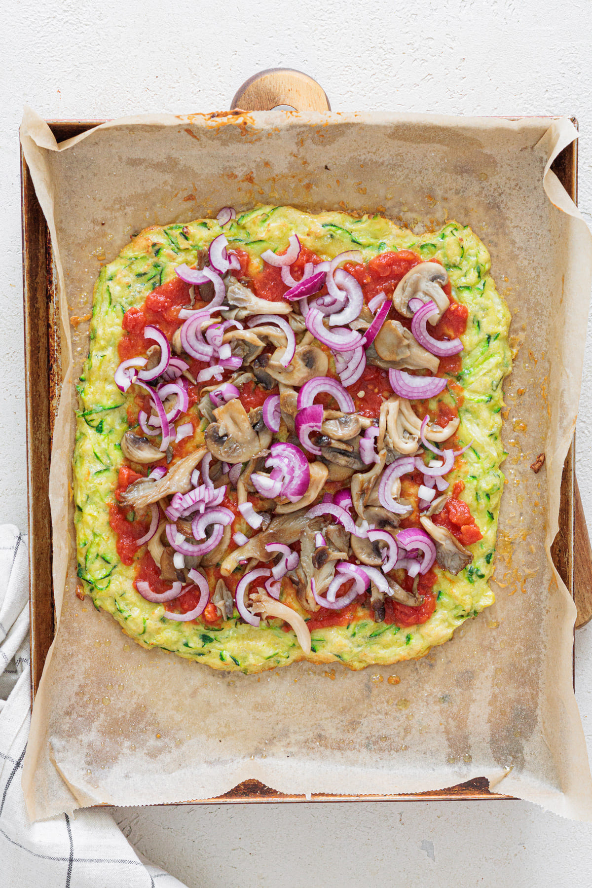 Zucchini crust pizza topped with tomato sauce, mushrooms, and sliced red onion