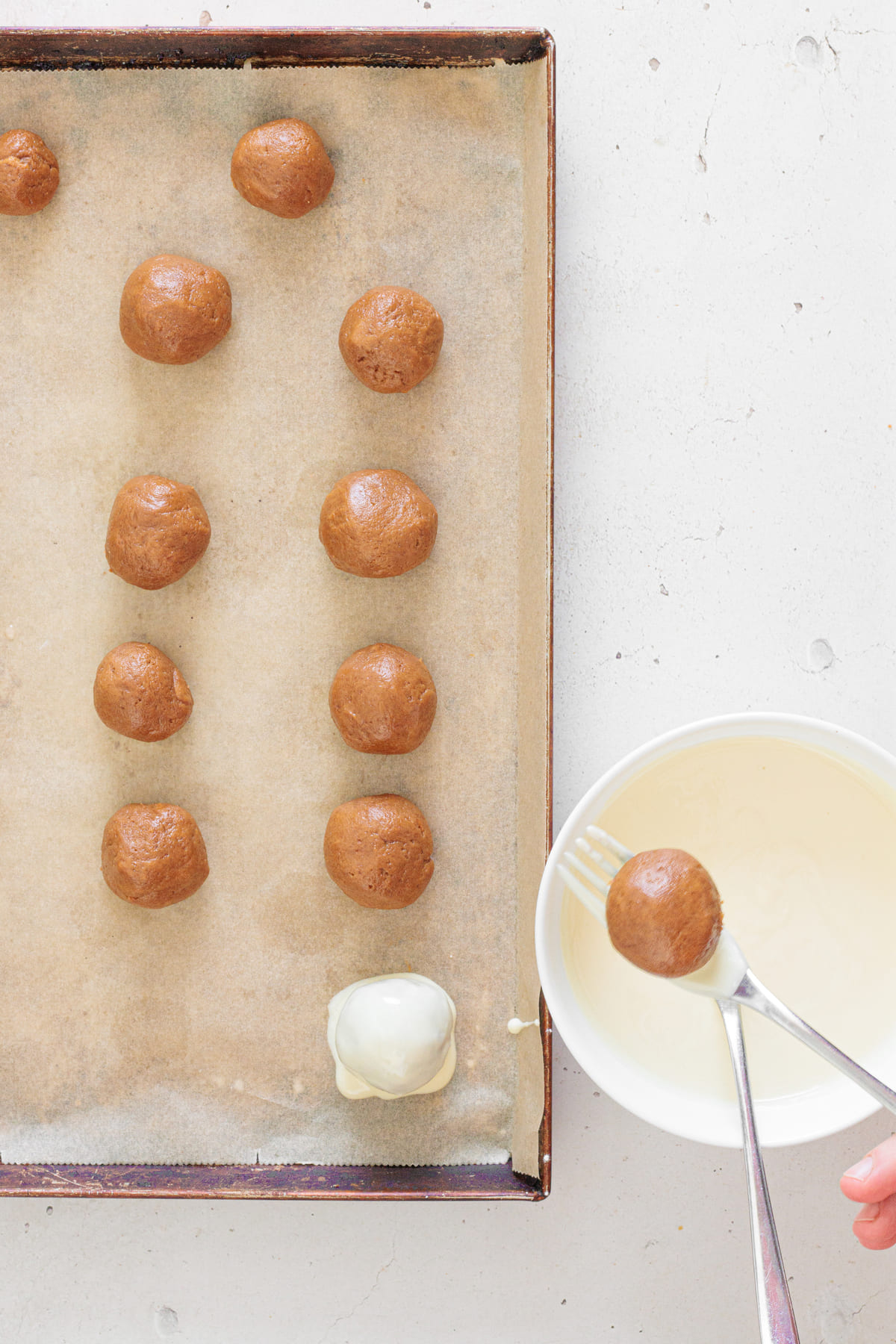Chilled gingerbread truffle balls on a tray with one ball being dipped into melted white chocolate.