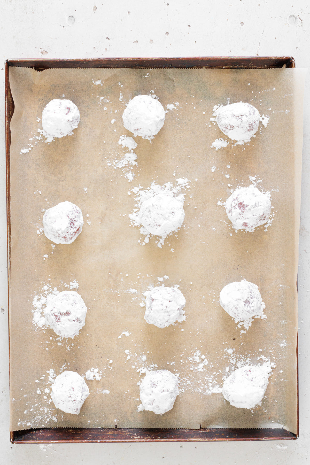 Red velvet cookie dough balls coated in sugar and arranged on a baking sheet.