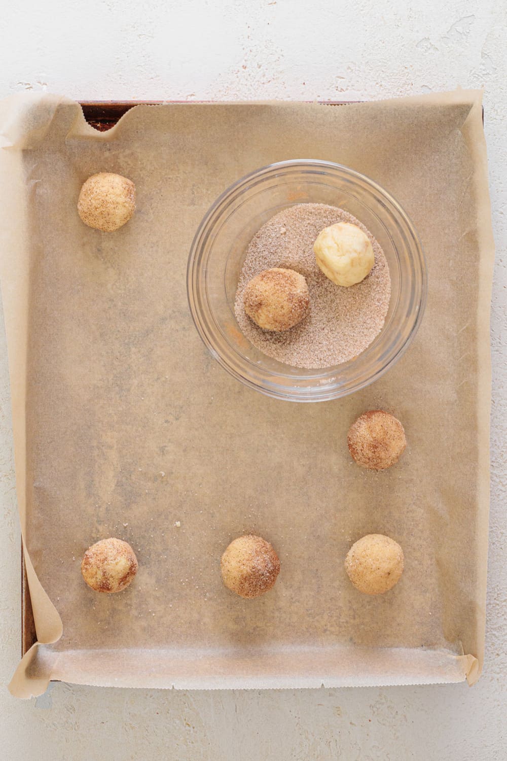 Scoop small portions of the cookie batter and roll them into balls, then fully coat them in the cinnamon sugar mixture.